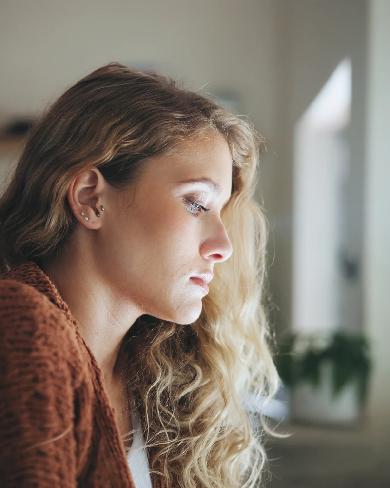 A woman seen in profile in soft window light, looking down, lost in thought