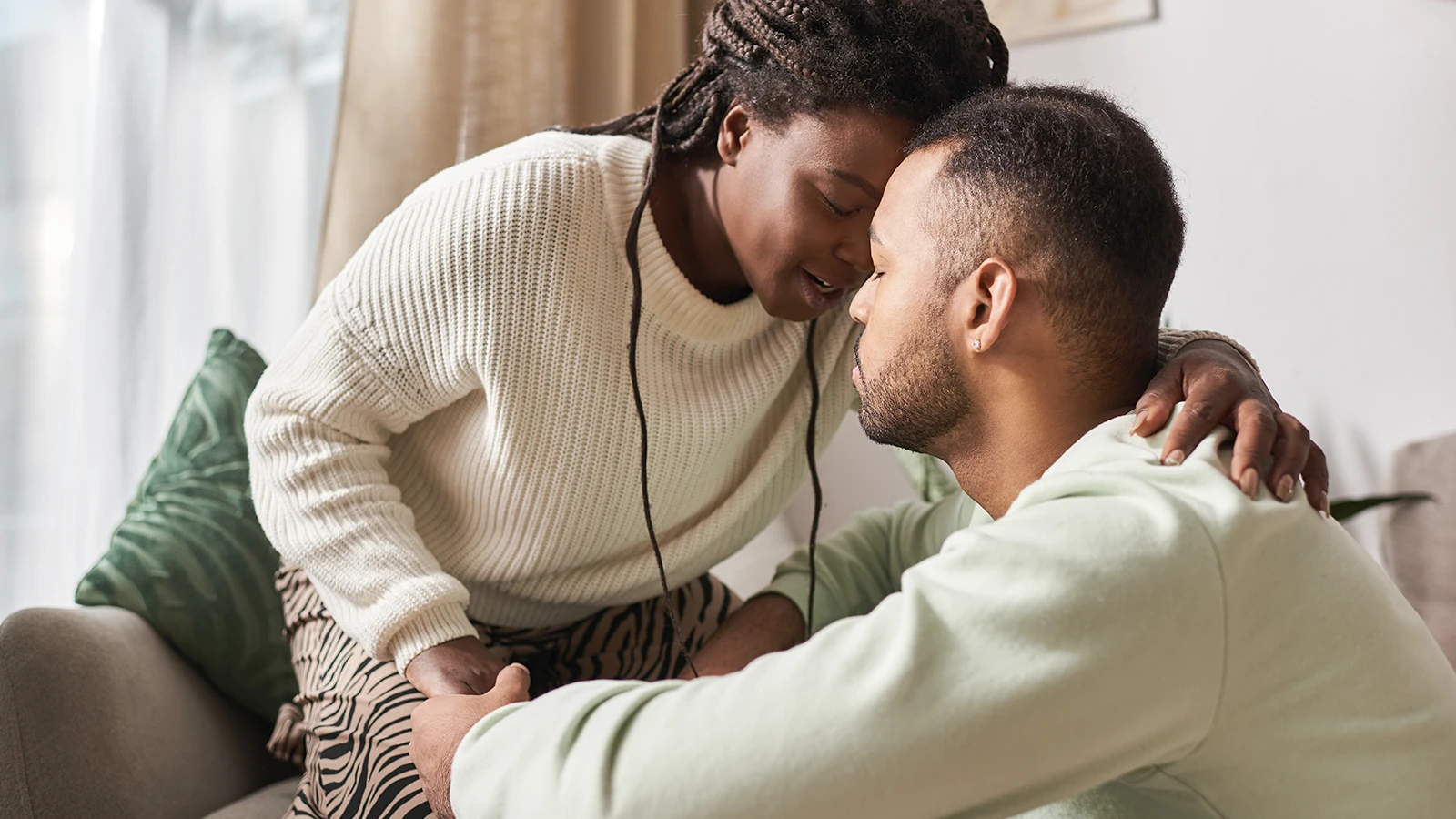 A couple on a sofa, foreheads touching, her arm around his shoulder
