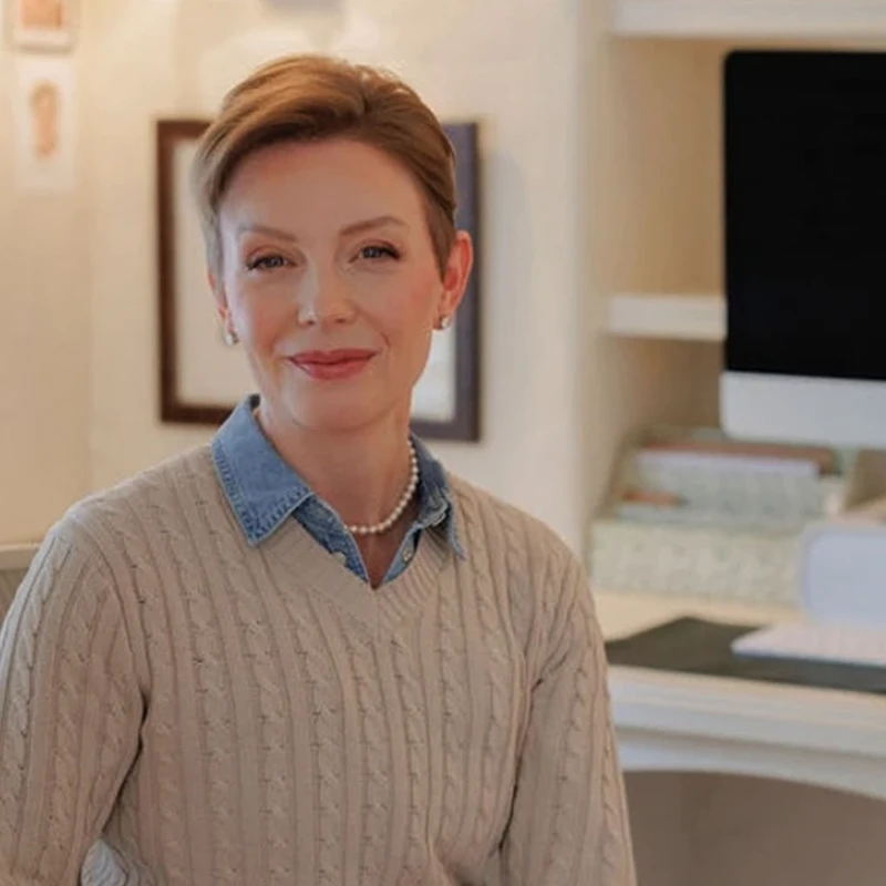 A smiling woman in a cable-knit sweater seated in a home office